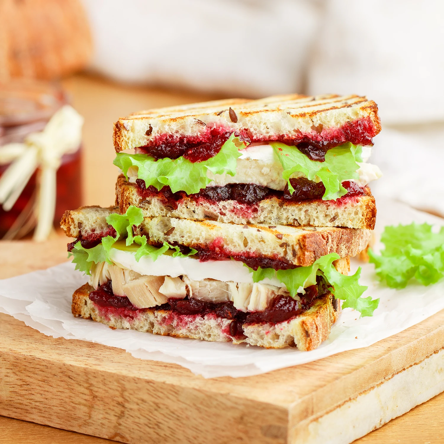 A Hovis Seed Sensations sandwich sliced in half and stacked on a plate, filled with cranberry sauce, lettuce leaves, turkey pieces and brie cheese.