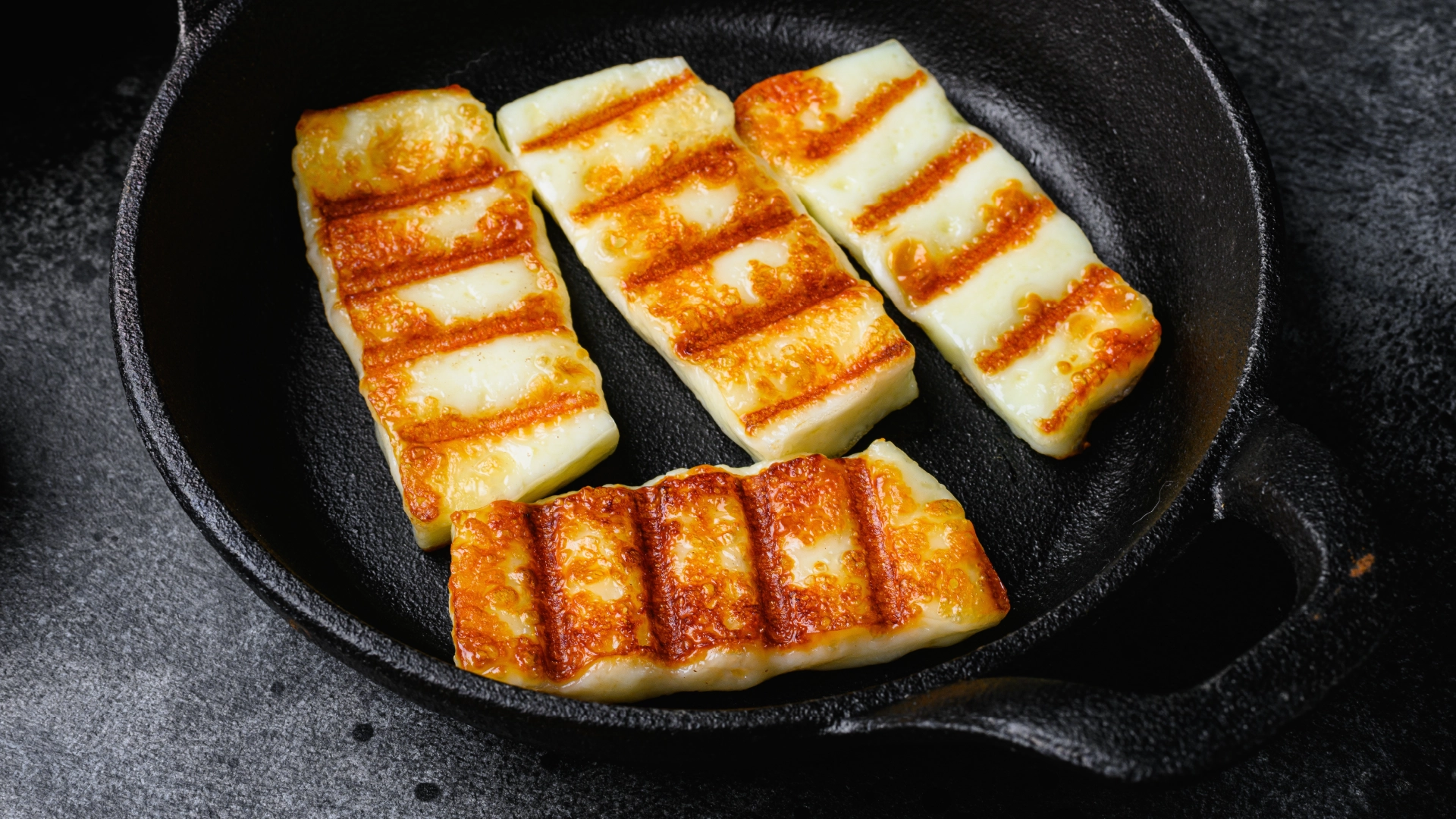 A frying pan with four slightly toasted slices of halloumi.