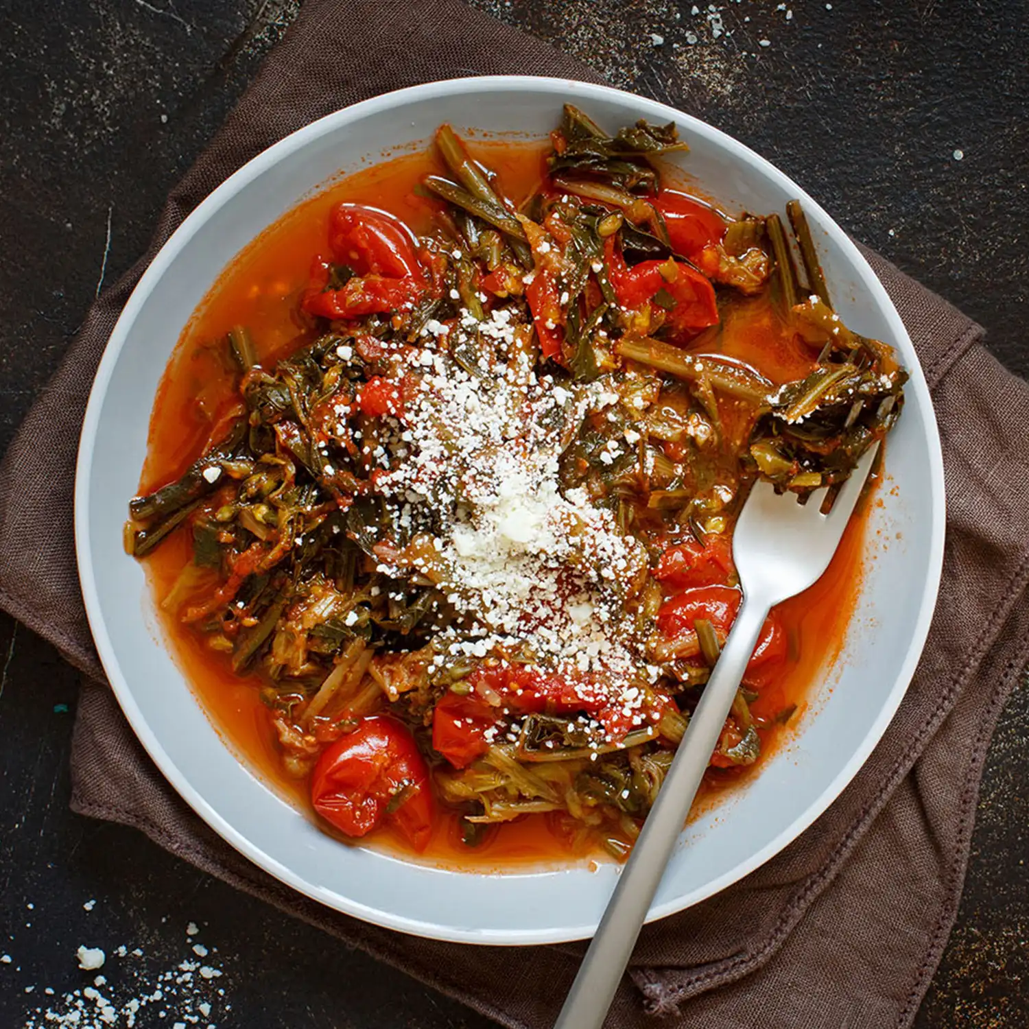 A top-down view of a white plate with Ribollita; featuring pieces of cooked vegetables and soaked bread pieces on top of a tomato sauce.