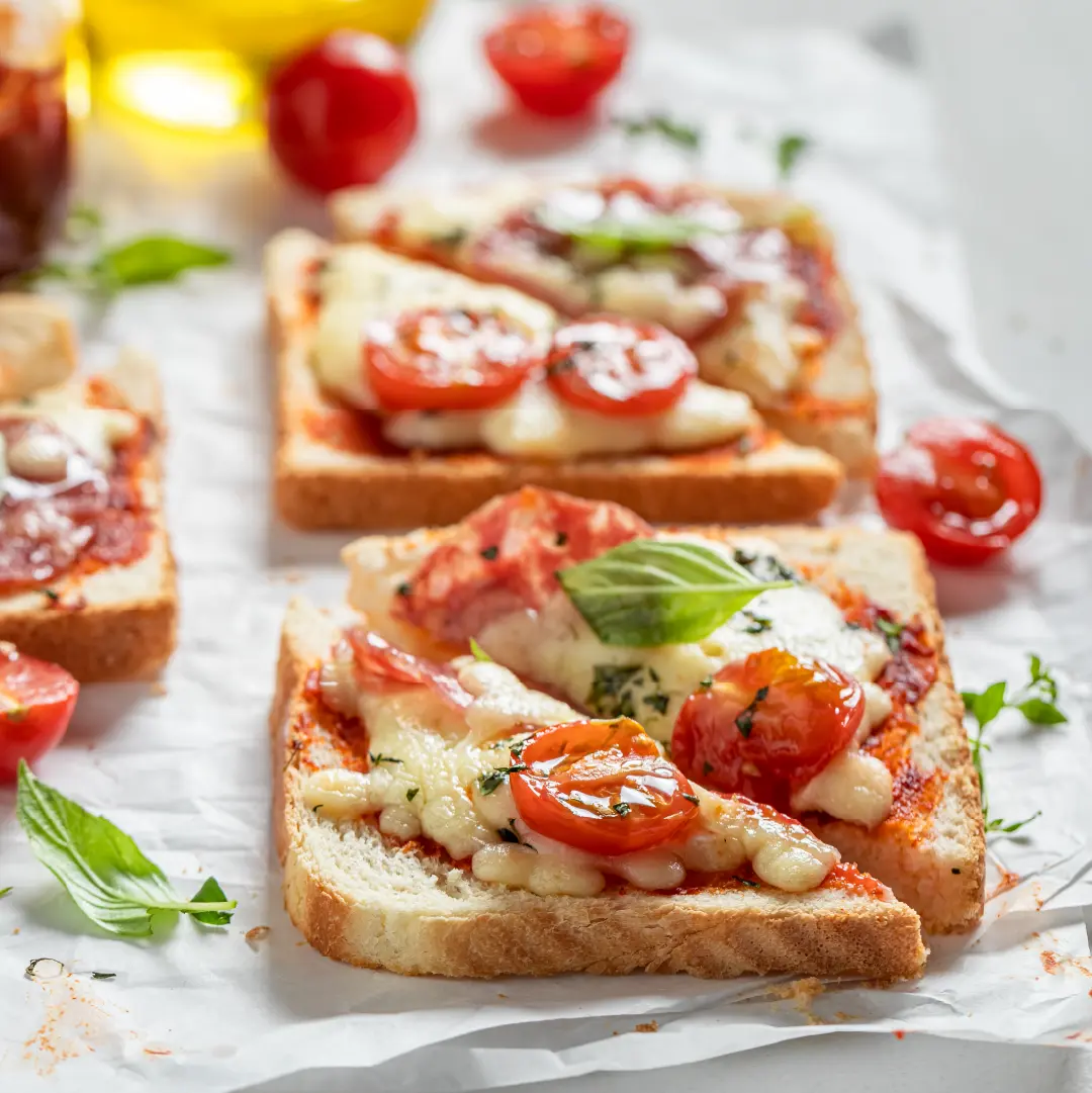 Two slices of toasted Hovis Farmhouse Batch, sliced in half, topped with molten cheese, sliced cherry tomatoes, and basil leaves.