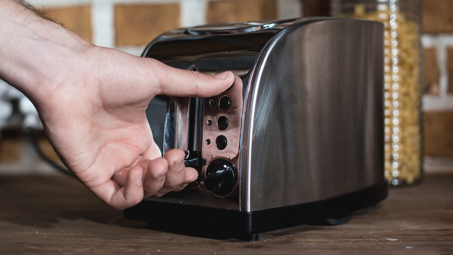 Someone using a silver toaster on a dark wooden counter.