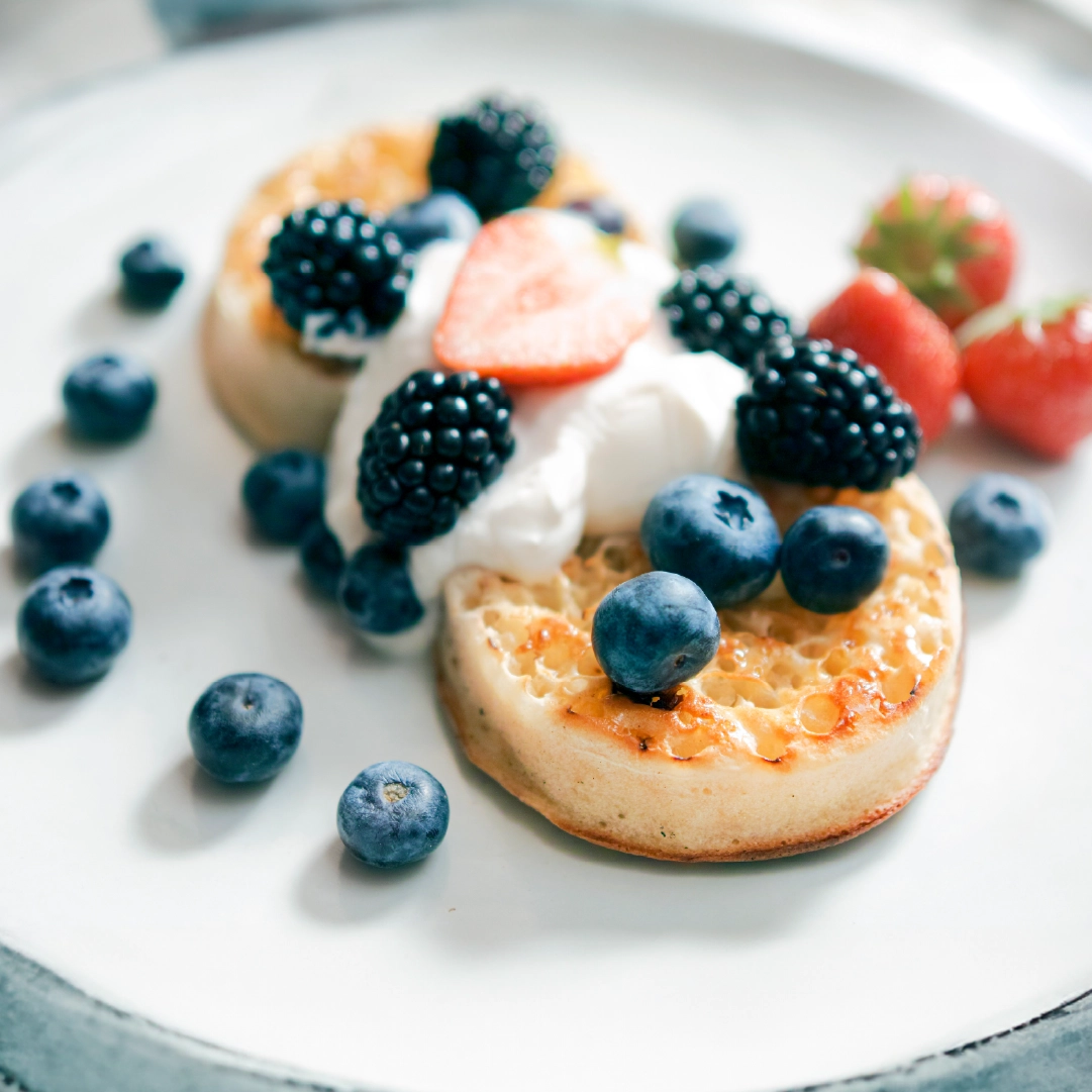 Two slightly toasted crumpets topped with Greek yogurt, blueberries, blackberries, and sliced strawberries.