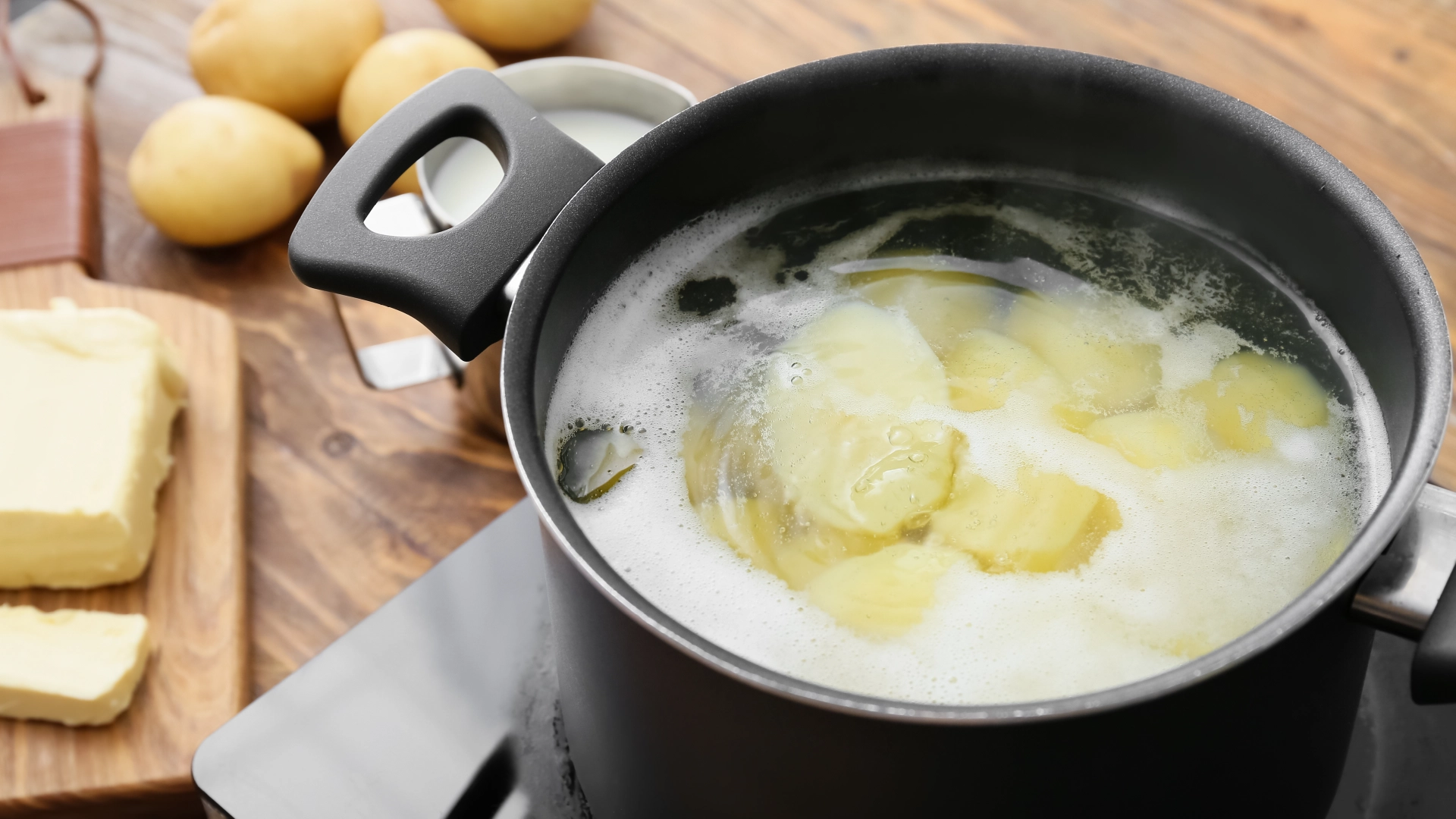 A large pot filled with simmering water and sliced potatoes cut lengthwise.