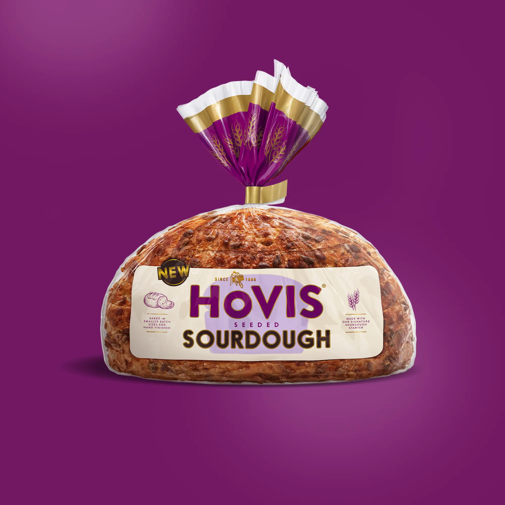 A loaf of Hovis Seeded Sourdough bread is displayed on a purple background. The packaging features a white and purple design with a gold trim and nutrition information. A 'NEW' label is shown on the top corner of the pack