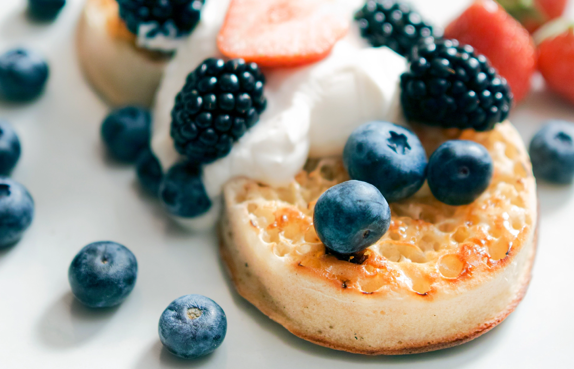 Two slightly toasted crumpets topped with Greek yogurt, blueberries, blackberries, and sliced strawberries.