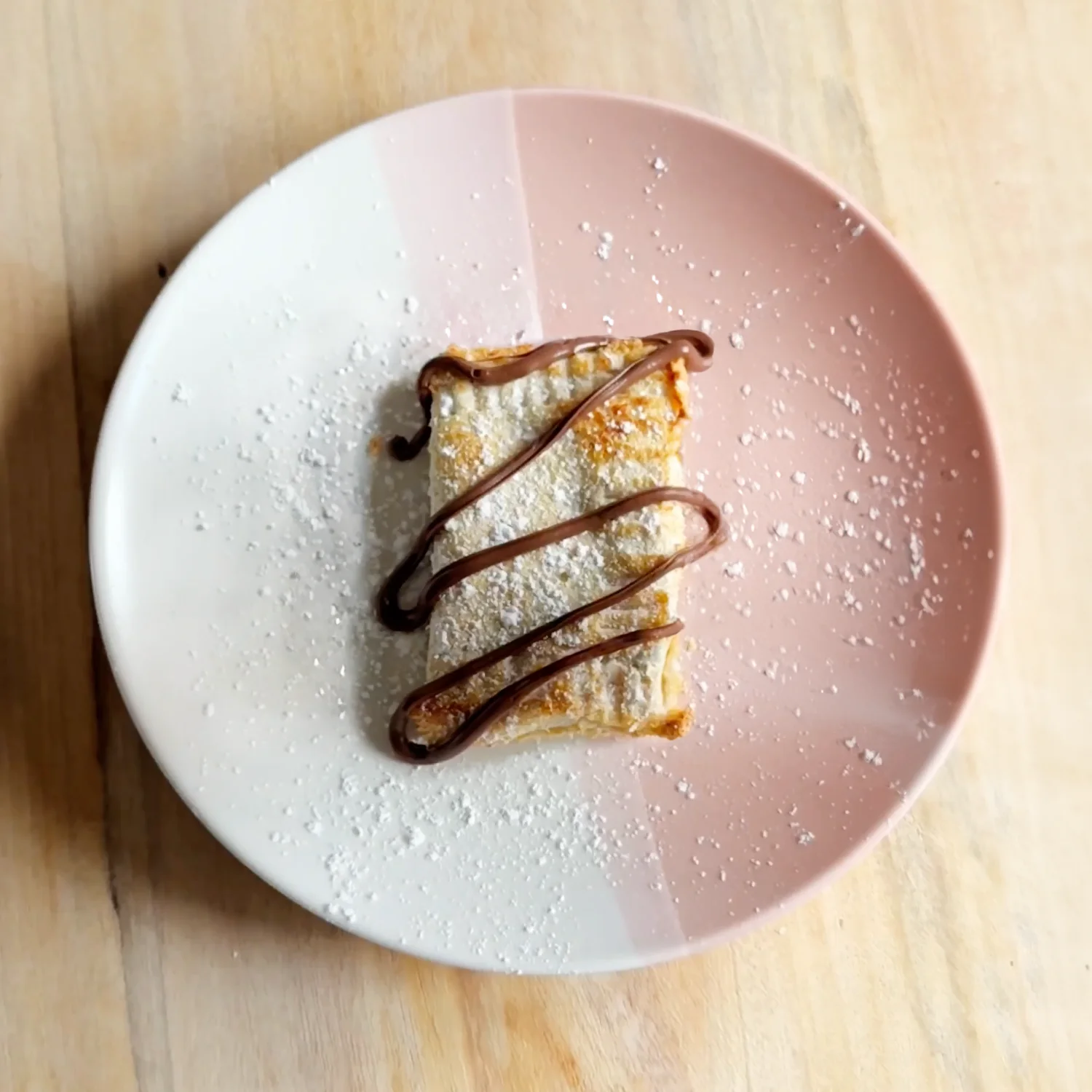 a sugar-dusted mini toasted chocolate pie on a pink and white plate, drizzled with chocolate