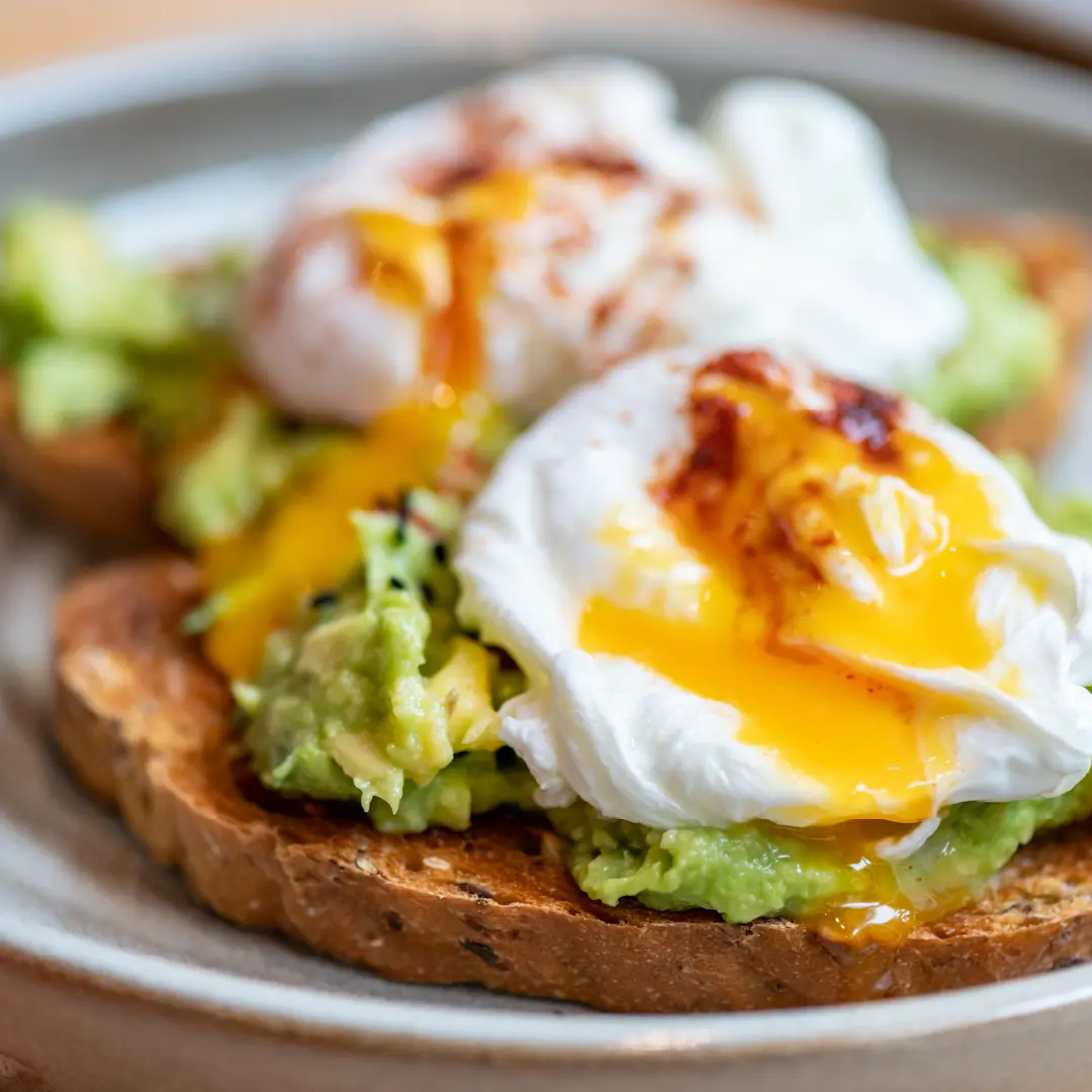 Two slices of slightly toasted seeded bread topped with mashed avocado, a poached egg, and a drizzle of chili oil.