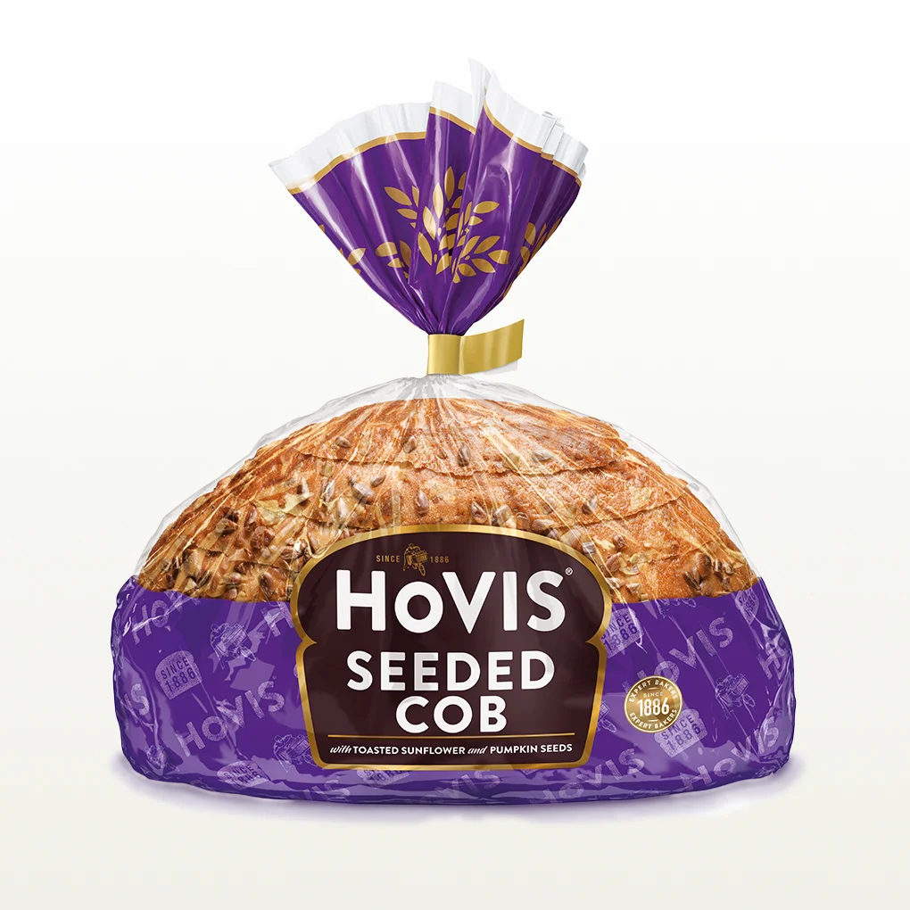 Hovis Seeded Half Cob bread on a white backdrop with a subtle shadow, featuring packaging decorated with a purple and the hovis logo