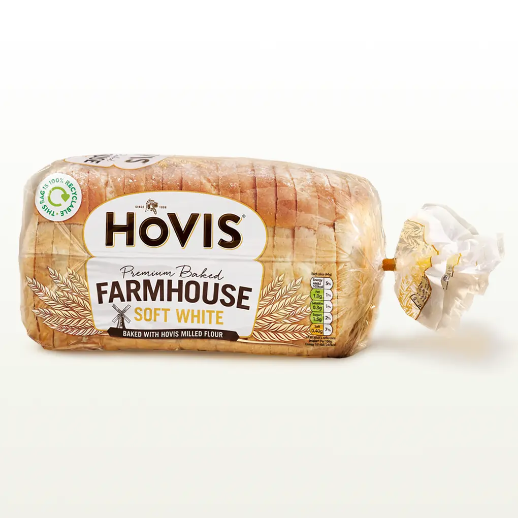 Hovis Farmhouse Soft White bread on a white backdrop with a subtle shadow. The packaging is transparent, decorated with wheats.