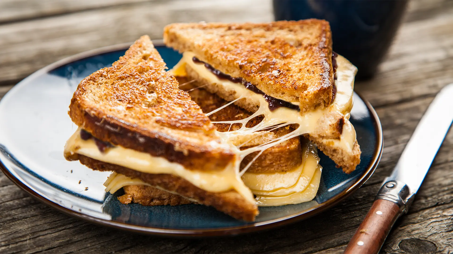 Two toasted sandwiches, stacked and sliced in half, with cheese oozing out.