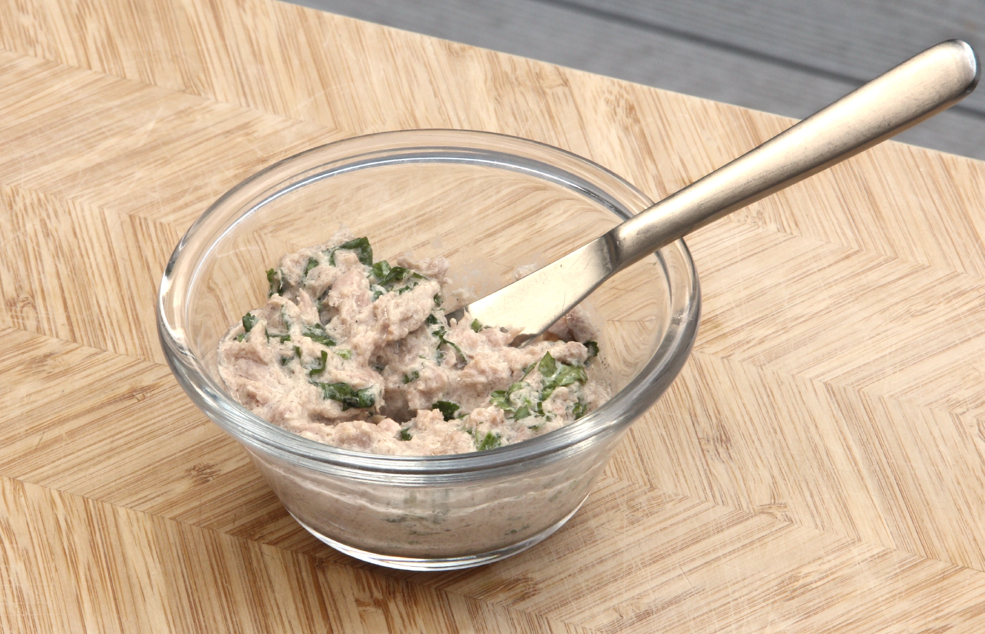 A small glass jar filled with a mix of tuna, mayo and chopped coriander, accompanied by a knife.