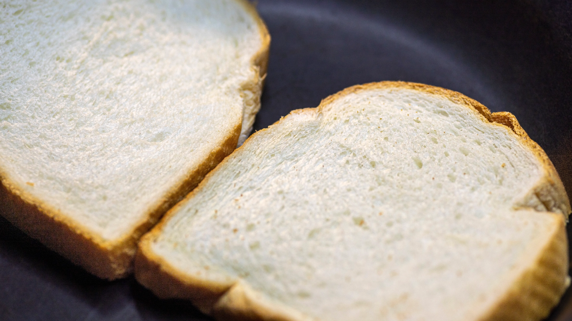 Two slices of white bread in a frying pan, about to be toasted