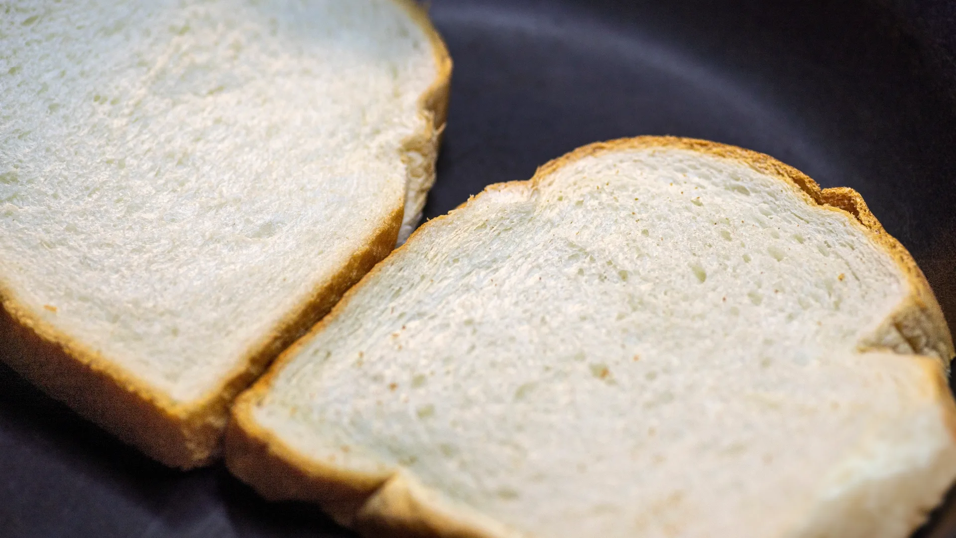 Two slices of Hovis Farmhouse Batch bread in a black frying pan, about to be toasted.