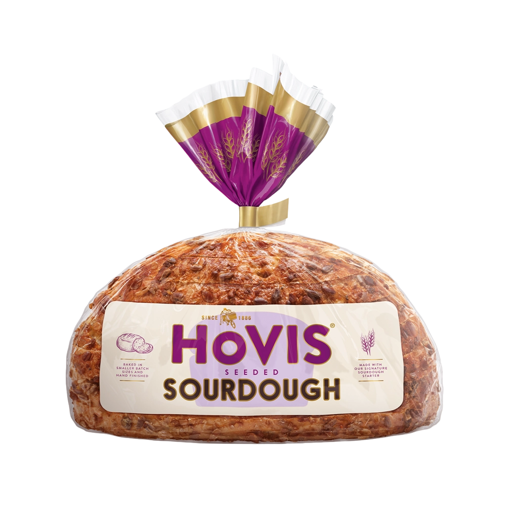 Hovis Seeded Sourdough bread on a white backdrop with a subtle shadow. The packaging is half transparent and half light and dark purple with gold detailing