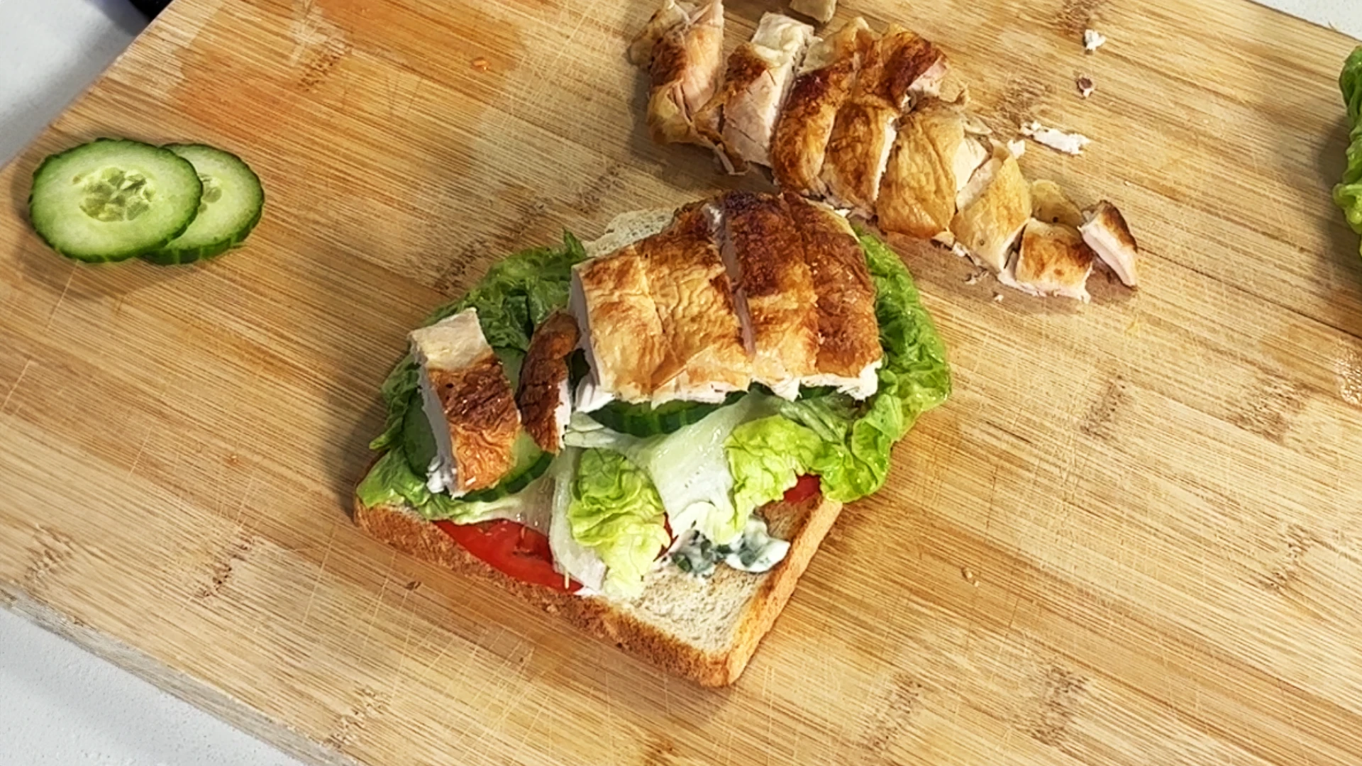 One slice of bread topped with tomatoes, salad leaves, and sliced chicken.