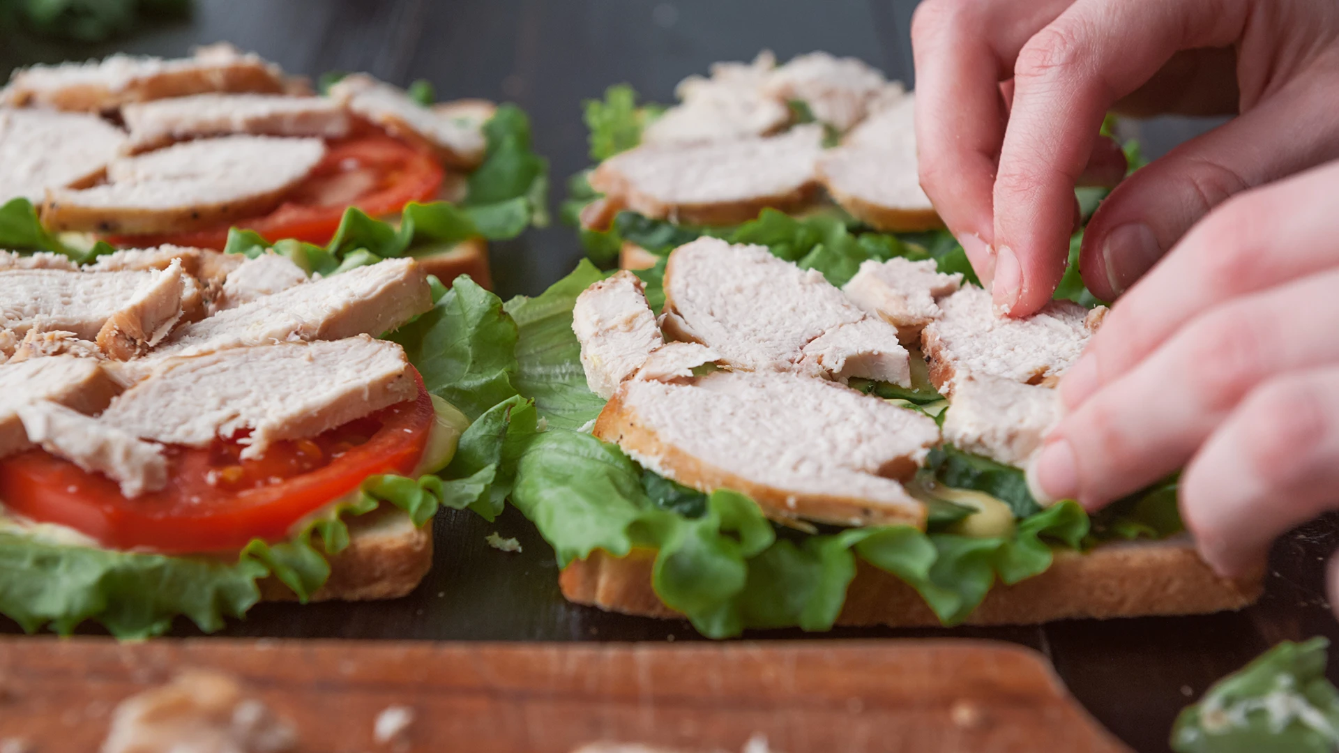 Someone is layering a sandwich with lettuce, tomato and chicken. 