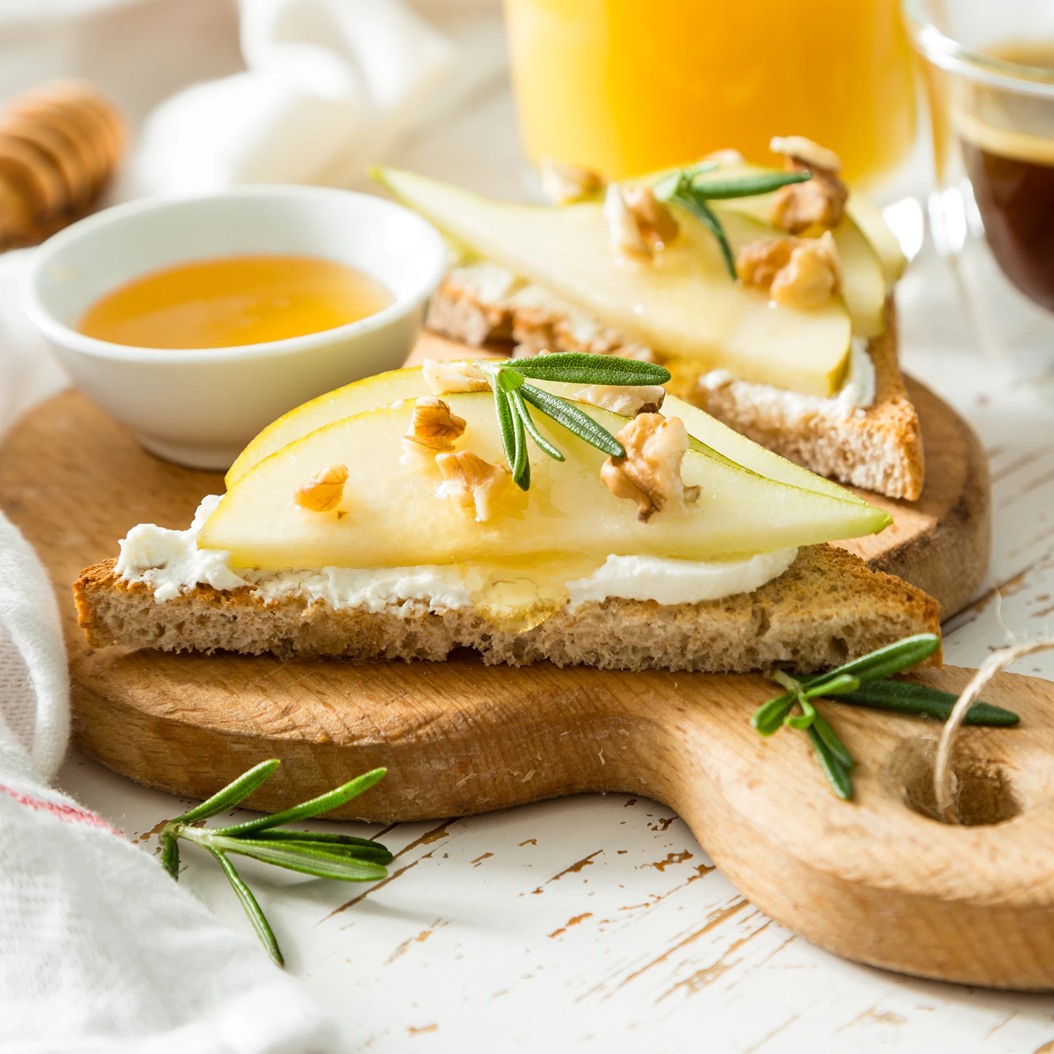 A slice of toast cut in half, topped with ricotta, two thin pear slices, and pieces of walnut on a wooden board.