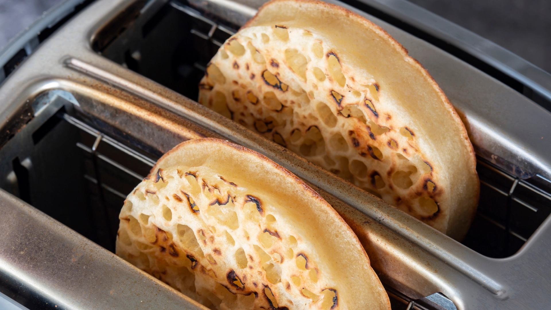 Two toasted crumpets coming out of a toaster.