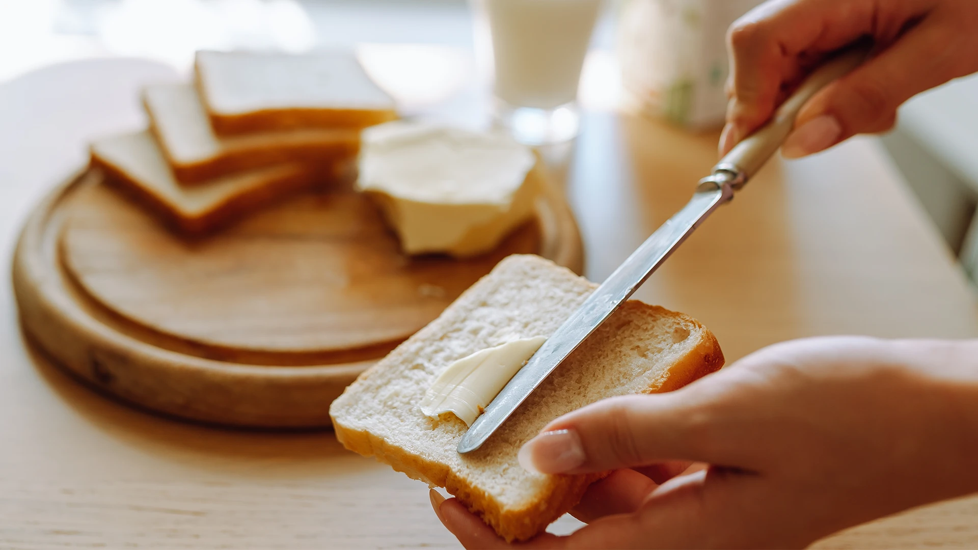 A slice of white bread being spread with butter using a knife.