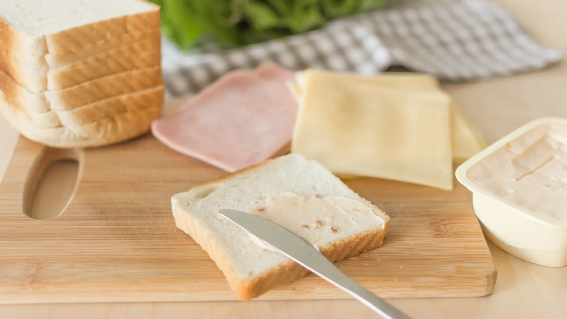 A knife spreading butter on a slice of white bread.