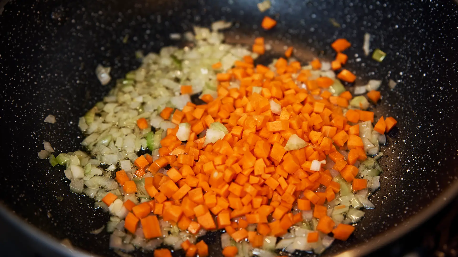 Diced onions, carrots, and celery are sautéed in a frying pan, glistening with olive oil, as the base for the ribollita.