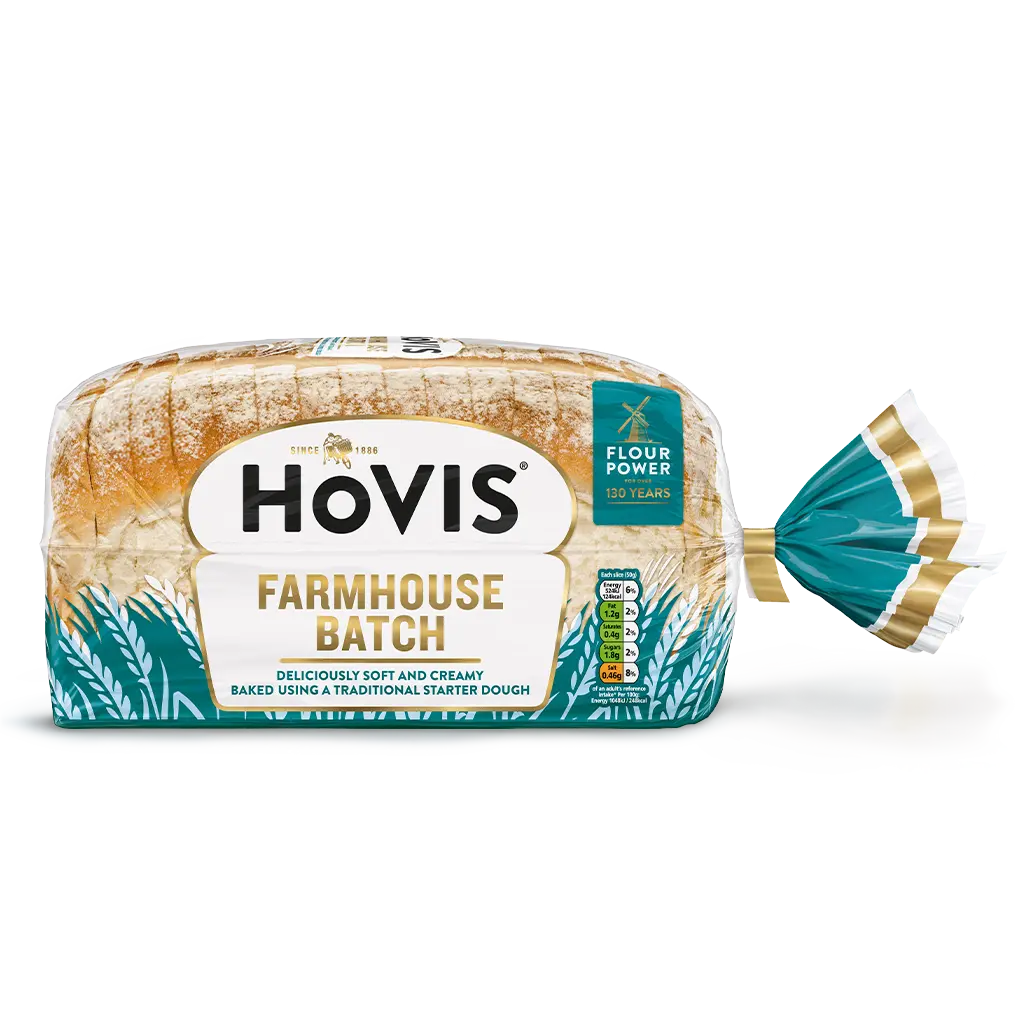 Hovis Farmhouse Batch bread with a subtle shadow under it. The packaging is half transparent and half dark teal, decorated with wheats.