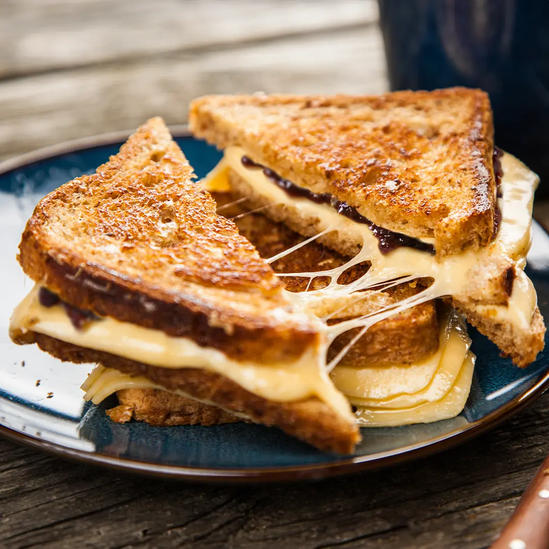 Two toasted sandwiches, stacked and sliced in half, with cheese oozing out.