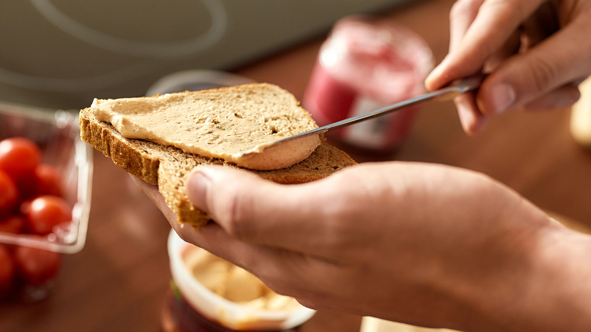 A slice of bread being spread with a spoonful of hummus