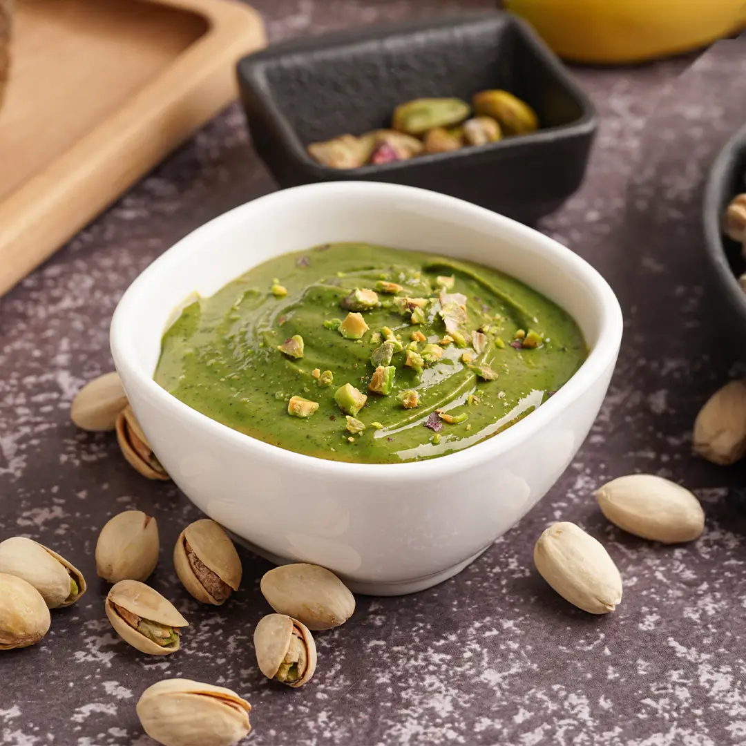 Matcha pistachio spread ingredients being blended in white food processor by a woman in a red top.