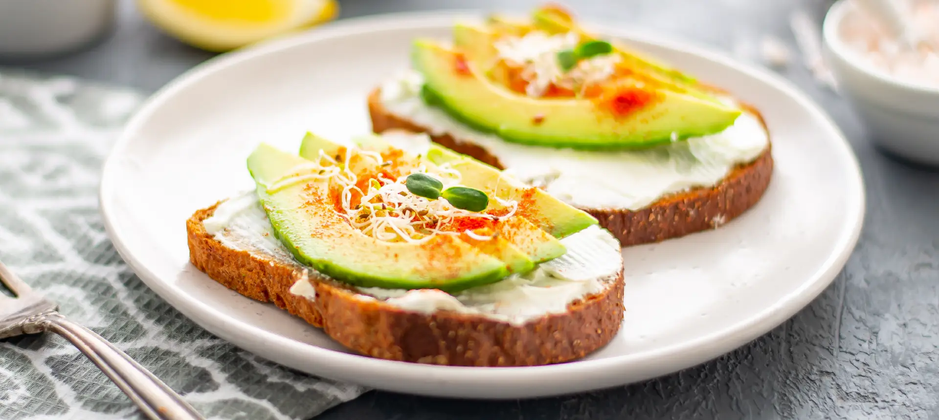 Two slices of Hovis Rustic Granary® Bloomer bread topped with cream cheese, thinly sliced avocado, cress, and a sprinkle of chili.