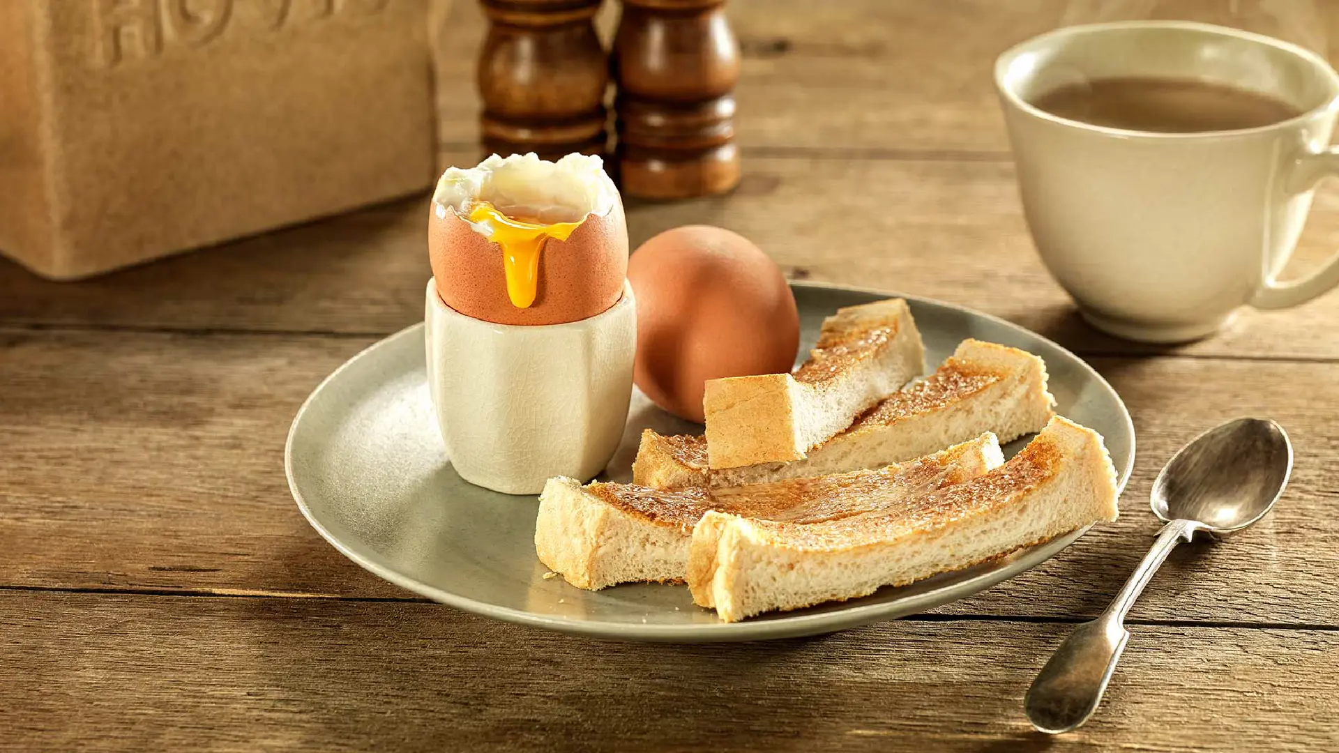 A soft-boiled egg with a runny yolk in an egg holder, with strips of toasted bread on the side.