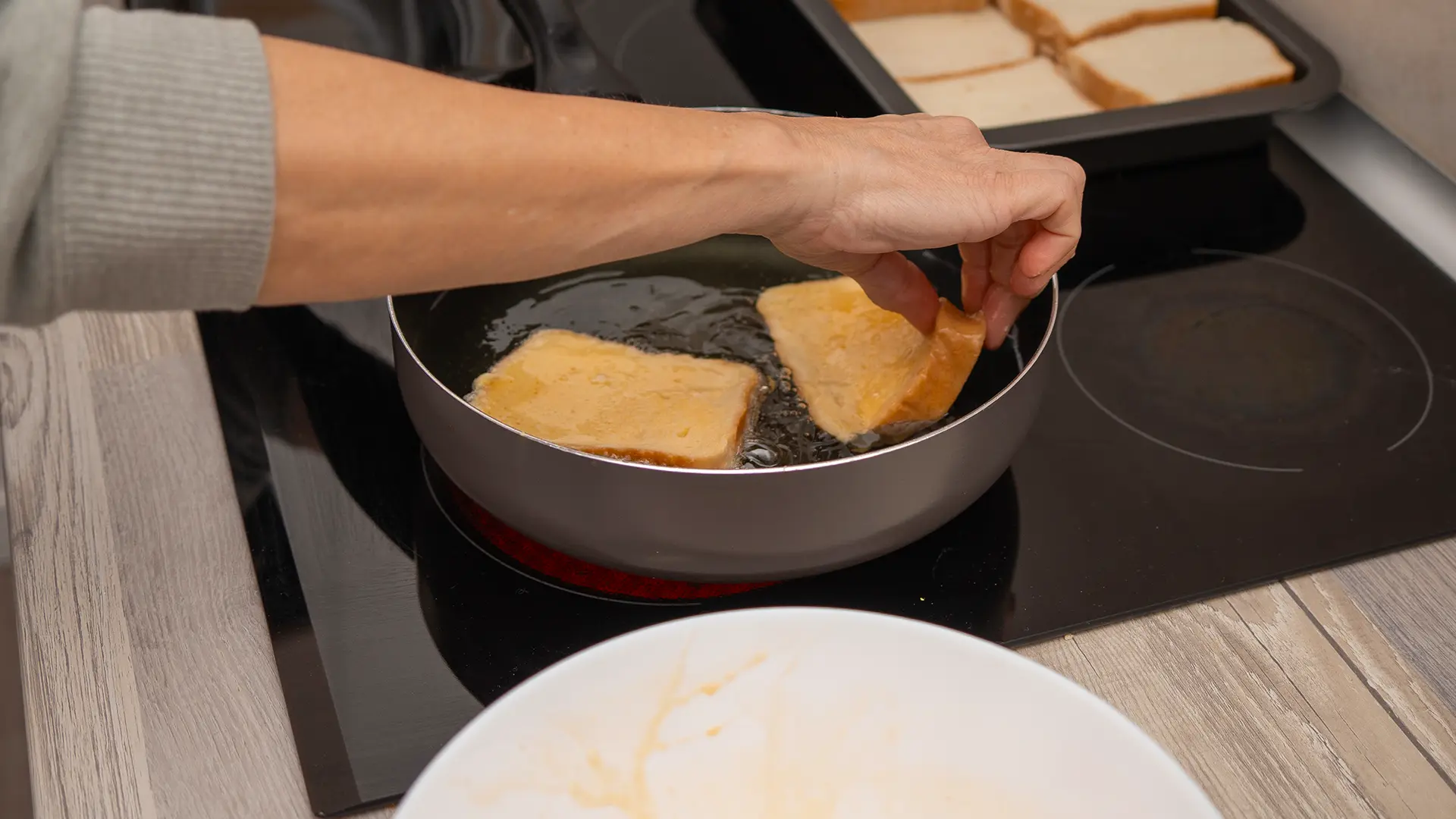 Egg-washed peanut butter sandwiches being lowered into a pan of hot oil for shallow frying.