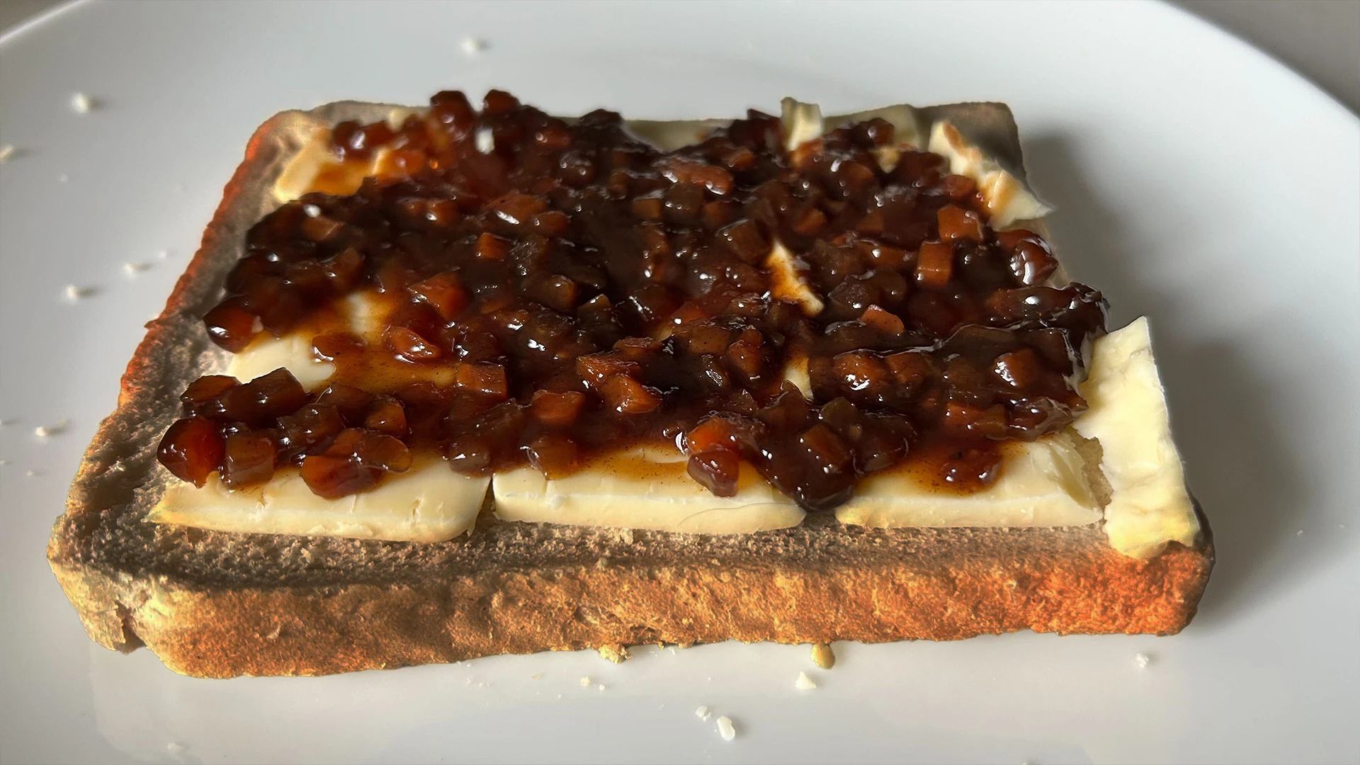 A slice of brown bread on a plate topped with slices of cheese and onion chutney.