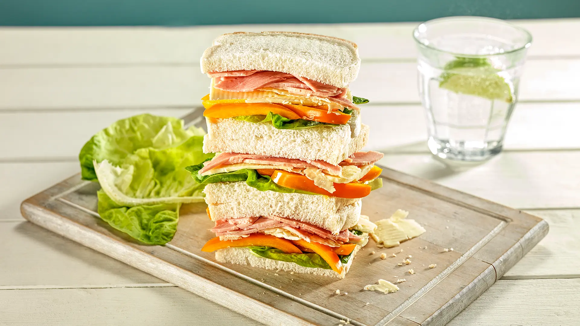 Three halves of a Hovis Soft White Medium 400g sandwich, stacked and filled with cheese, ham, pepper, and lettuce leaves.