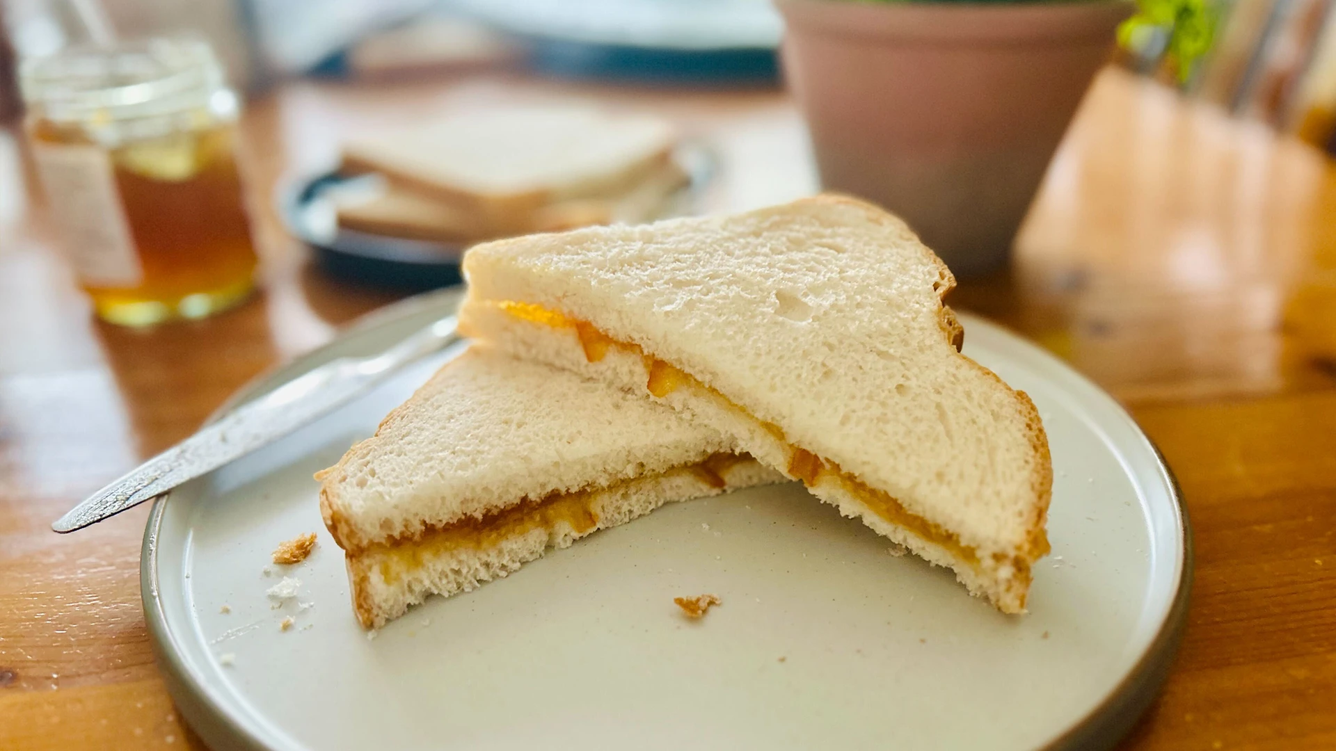 A Marmalade Sandwich cut into triangles sits on a wooden table. The sandwich is made using Hovis Farmhouse Batch.