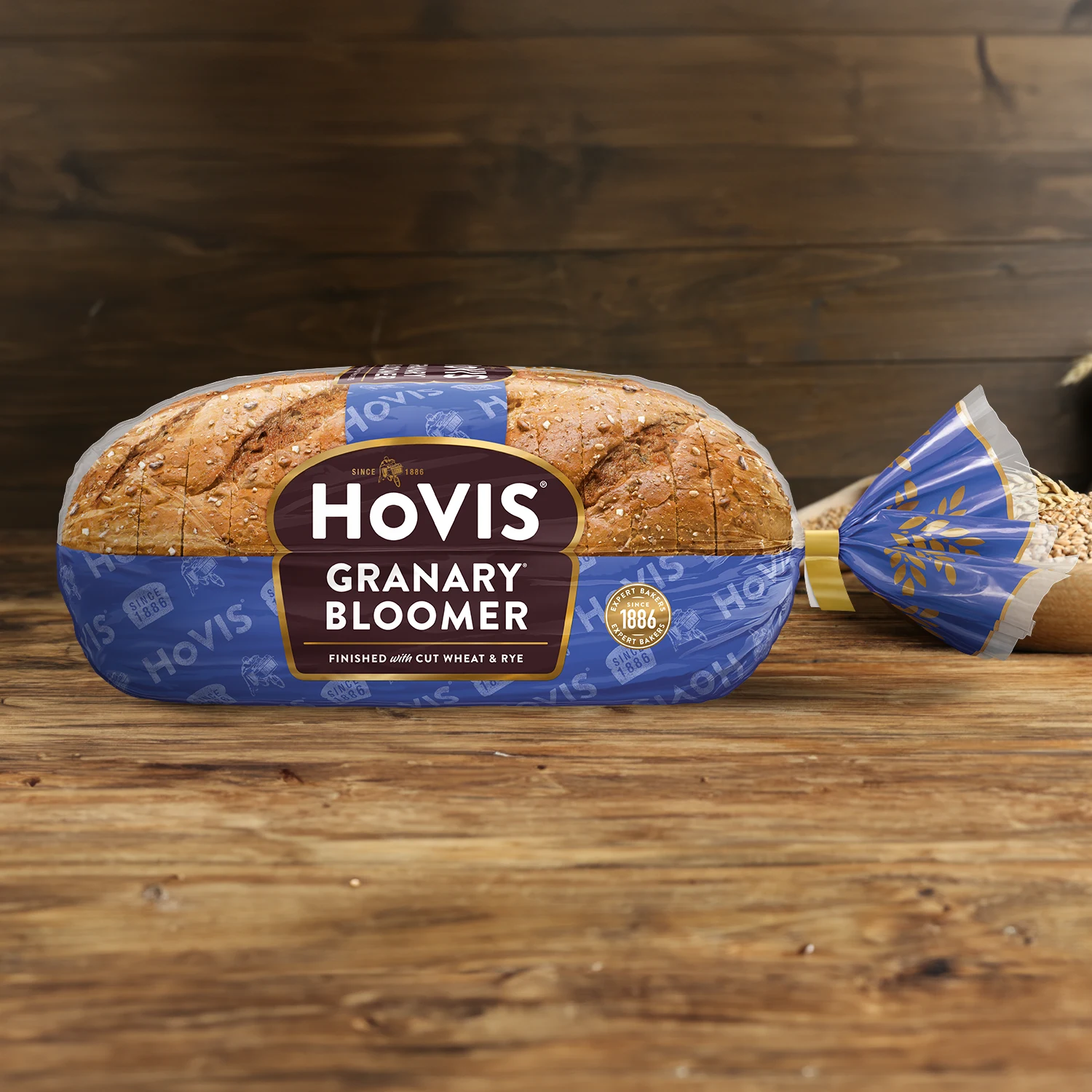 Hovis Granary Bloomer on a wooden table, with a bowl of wheat grains, a wooden scoop, and dried wheat in the background.