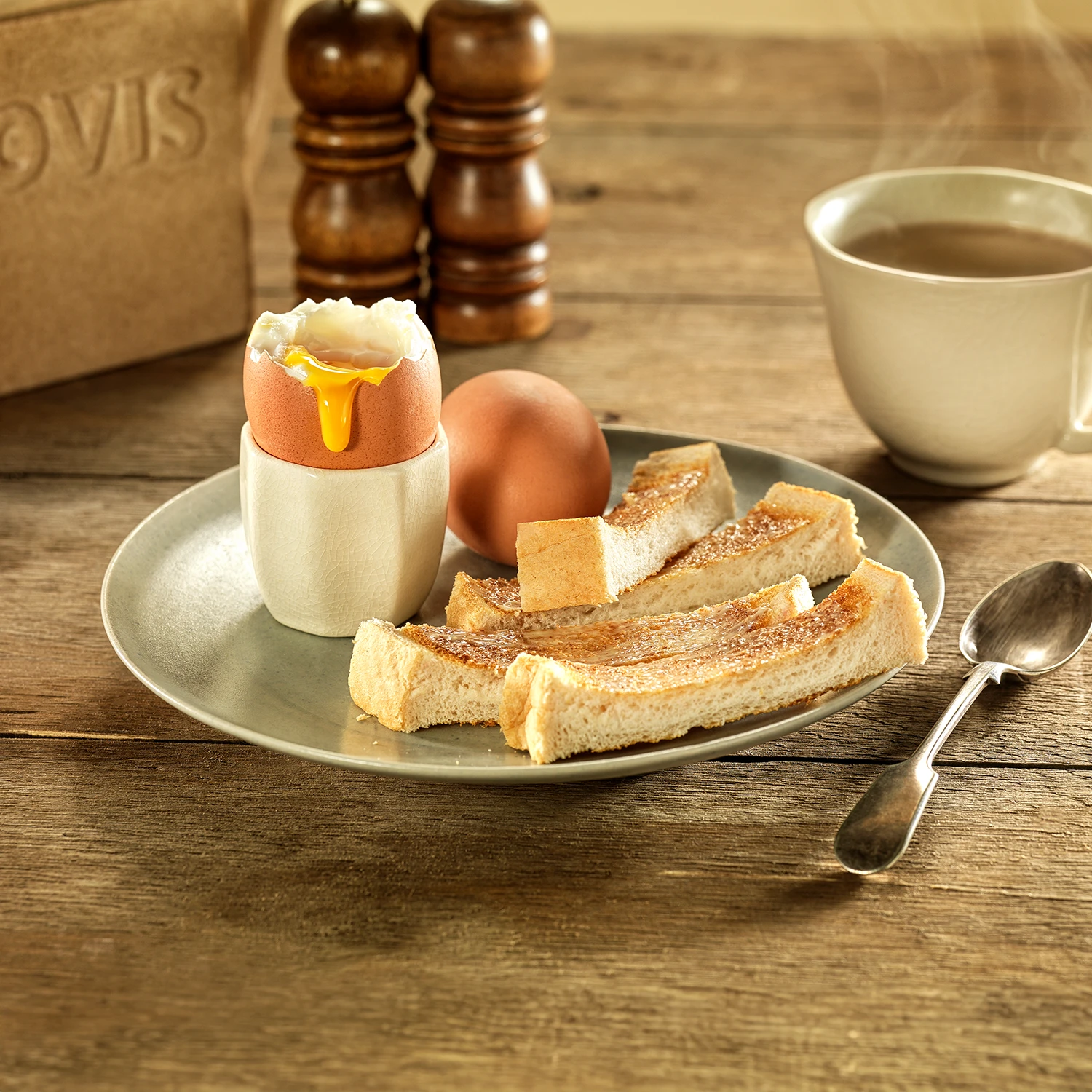 Strips of toasted Hovis Soft White Extra Thick bread alongside a soft-boiled egg with a runny yolk in an egg holder, with a spoon on the side.