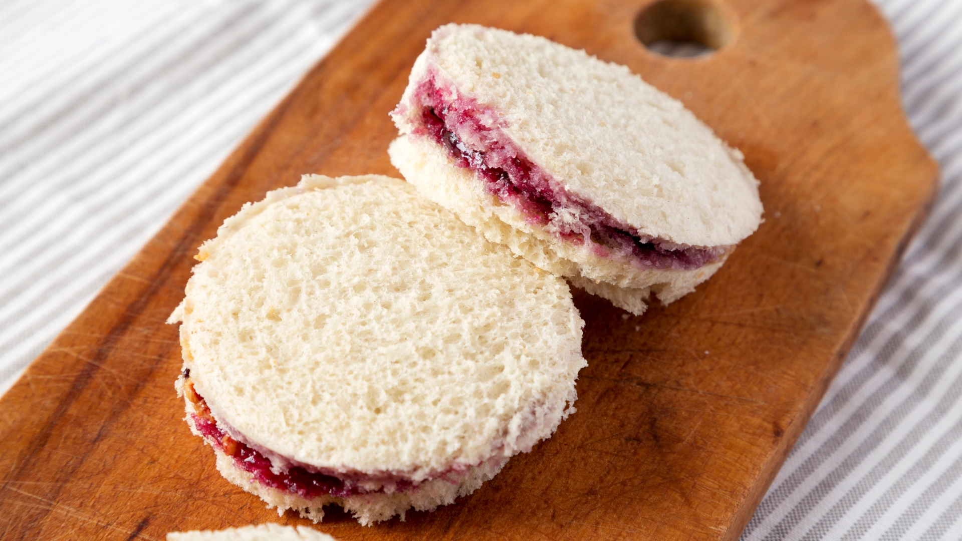 Two small, circular jam sandwiches placed on a wooden chopping board, with the jam slightly visible between the slices of bread.