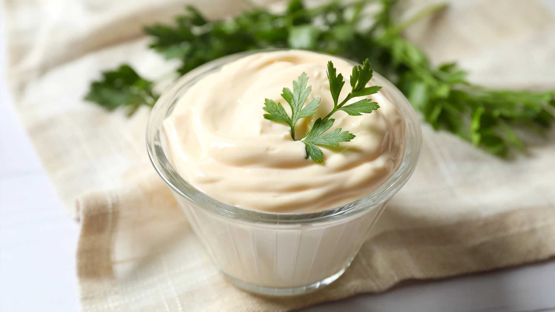 A bowl of mayonnaise with a parsley leaf on top.