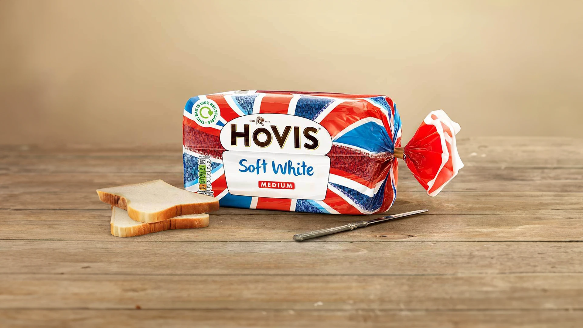 Hovis Soft White bread inside its Union Jack-inspired packaging, with two slices of bread and a metal knife beside it.