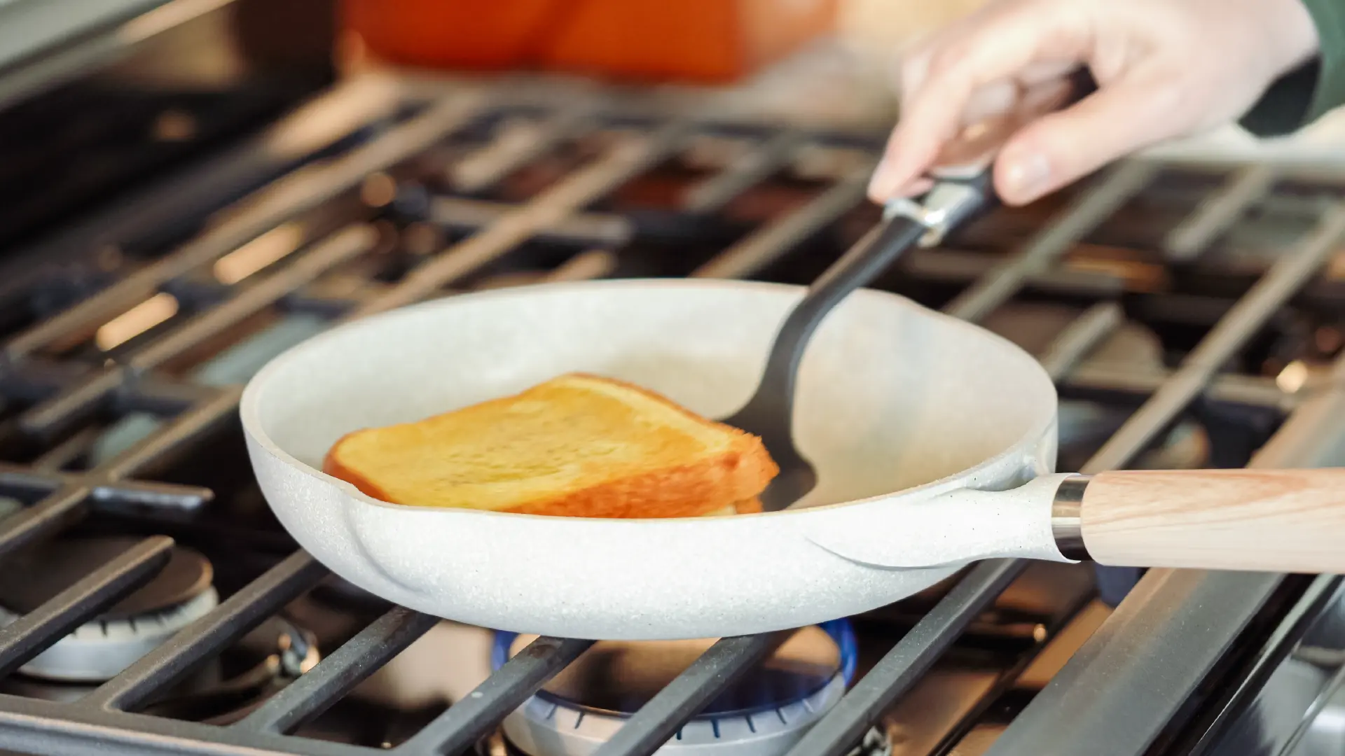 A slightly toasted sandwich in a pan on the hob, with a hand holding a spatula, about to flip the sandwich.