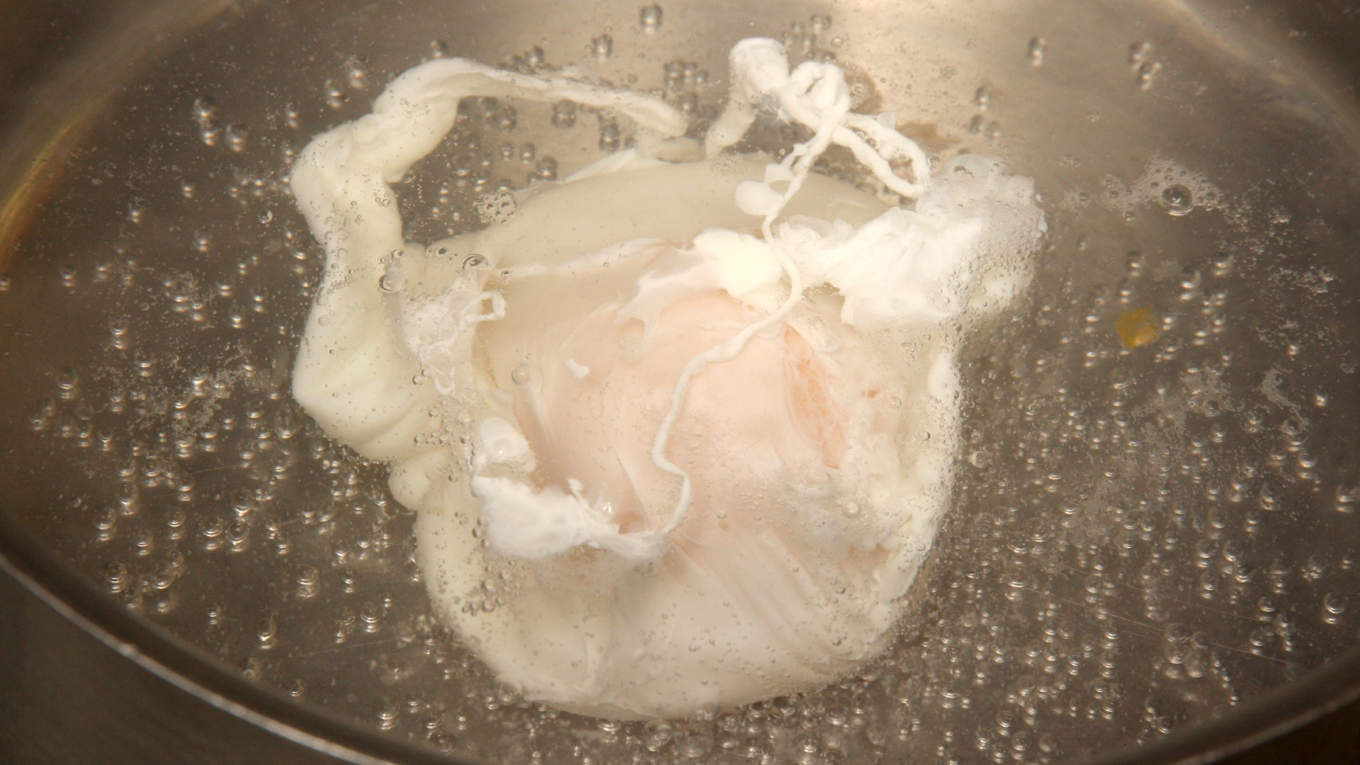 A poached egg simmering in a metal pot full of boiling water.