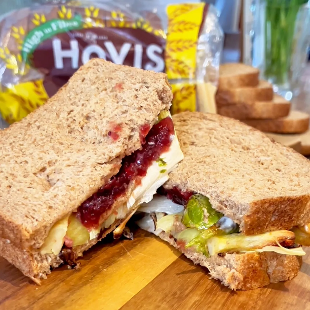 A left over christmas sandwich sits on a wooden chopping board in a kitchen