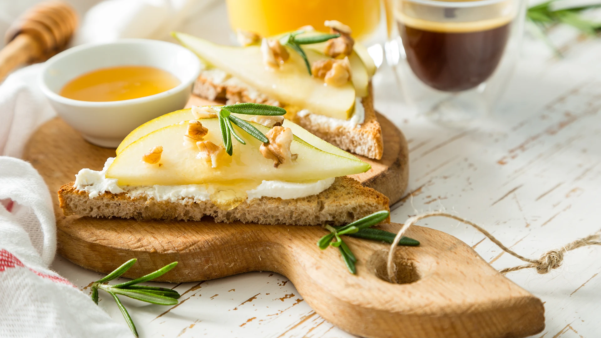 A slice of toast cut in half, topped with ricotta, two thin pear slices, and pieces of walnut on a wooden board.