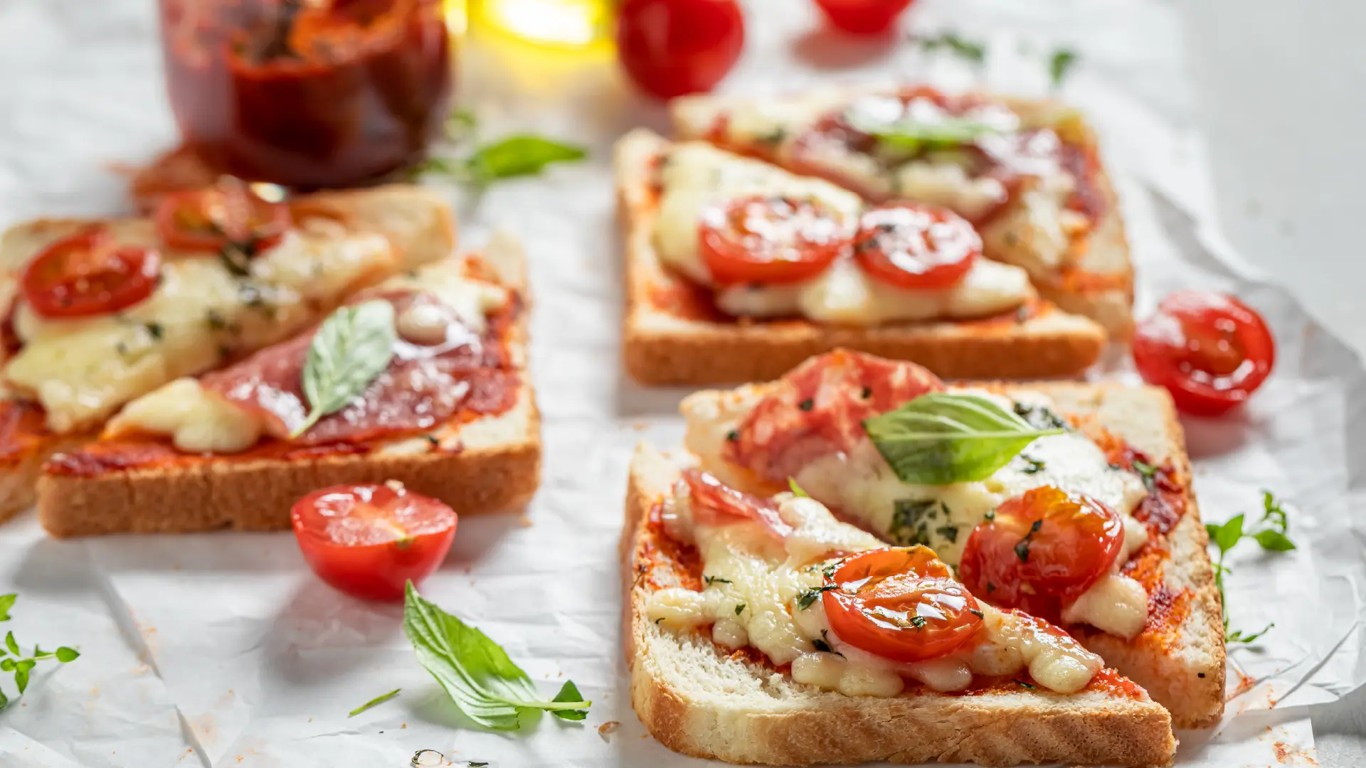 Two slices of toast, sliced in half, topped with molten cheese, sliced cherry tomatoes, and basil leaves.