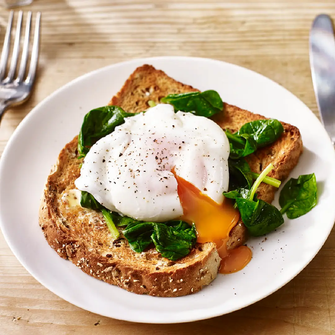 A toasted slice of bread on a plate, topped with wilted spinach and a perfectly poached egg, with the runny yolk spilling over the toast.