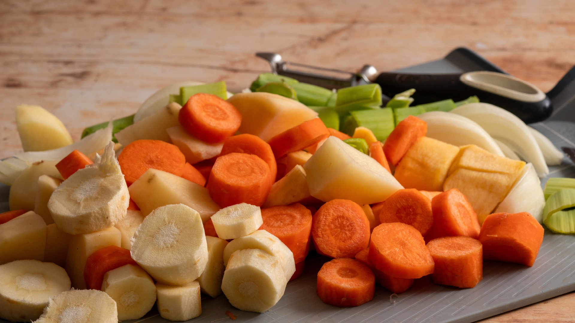 A chopping board topped with thick, round slices of carrots, parsnips, and celery.