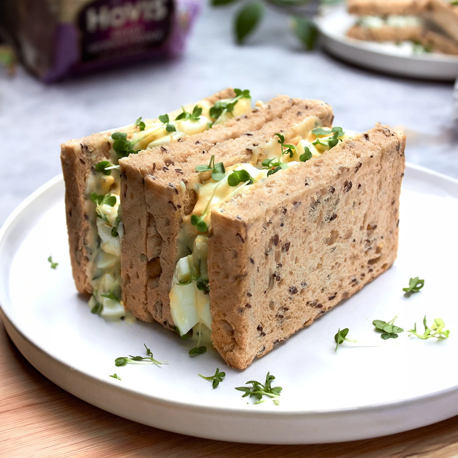 A plate with a sandwich cut in half made of seeded bread, filled with egg mayonnaise and cress.