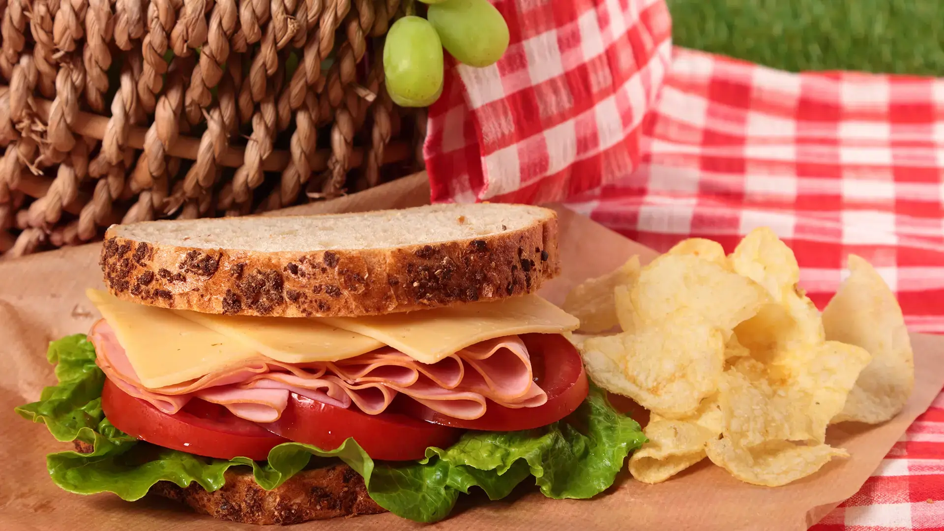 A sandwich on top of a picnic towel, with some crisps on the side.