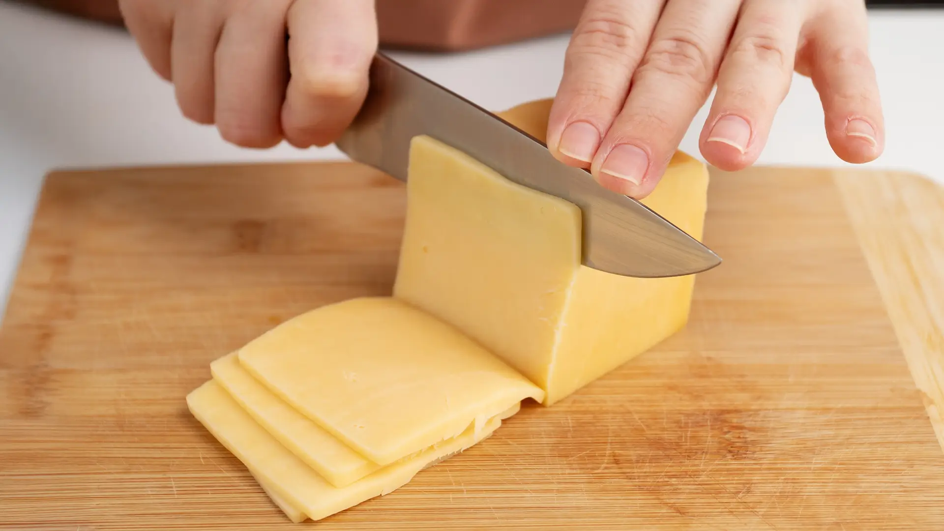 A knife is near a block of mozzarella cheese on a wooden chopping board. Some smaller pieces of the cheese have already been cut and are placed on the side.